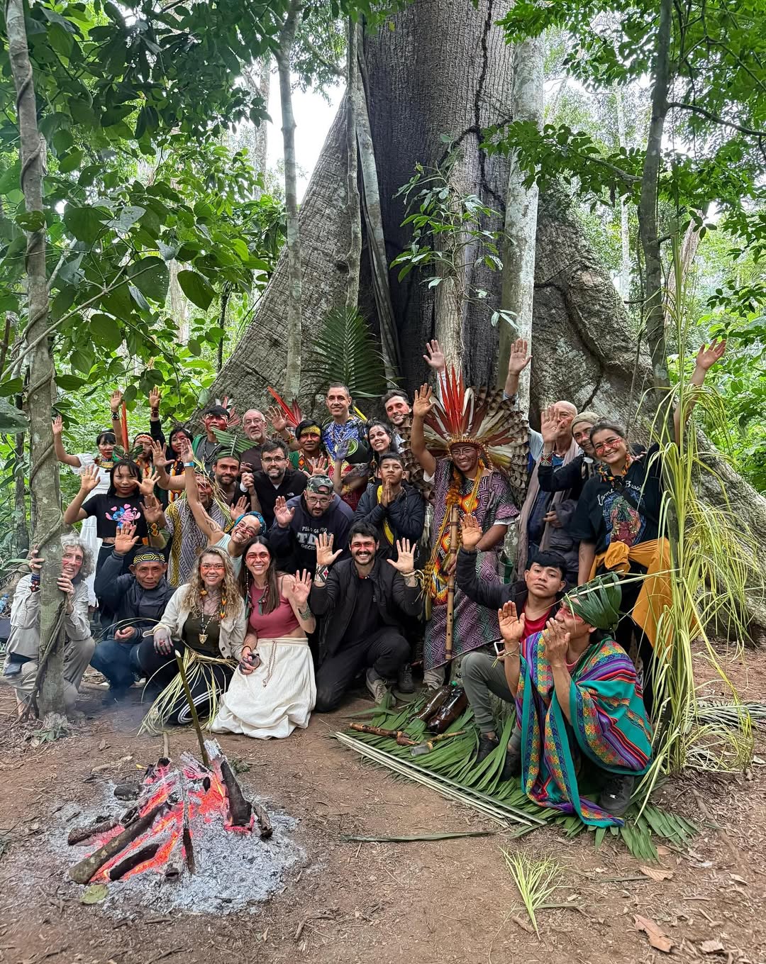 Indigenous tribe members and retreat participants gathered around a fire beneath a sacred tree in the Amazon rainforest of Acre, Brazil